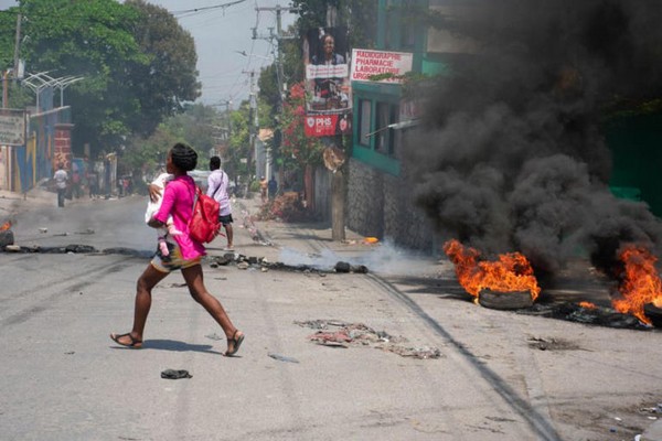 Photo de femme hatienne fuyant et portant son enfant  travers la rue pour chapper aux troubles en mars 2024...