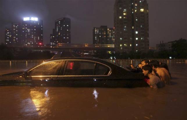 2) effet du dérèglement climatique : inondations records Photo de gens poussant une voiture dans une cité inondée