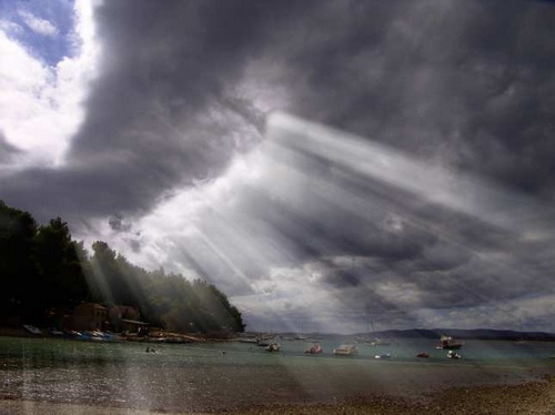 photo de clair obscur par rayons passant  travers nuages sombres sur rivage.