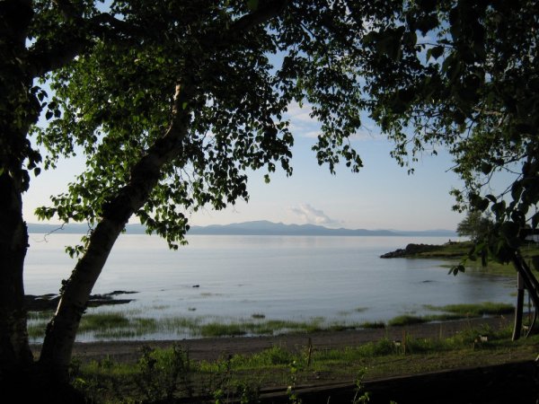 Dans son ciel tout bleu, un nuage flotte....Il passe lentement au-dessus du fleuve... Photo de rive du fleuve Saint-Laurent entre arbres, avec nuage et monts au loin.
